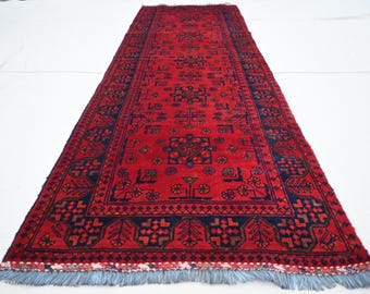 May include: A red and blue patterned rug with a geometric design. The rug has a fringe border and is made of wool.