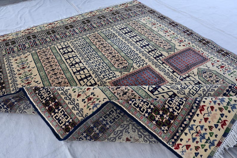 Pu&ograve; includere: Un tappeto beige e crema con un motivo geometrico in tonalit&agrave; di blu, verde e rosso. Il tappeto &egrave; piegato a met&agrave; e ha frange sui bordi.