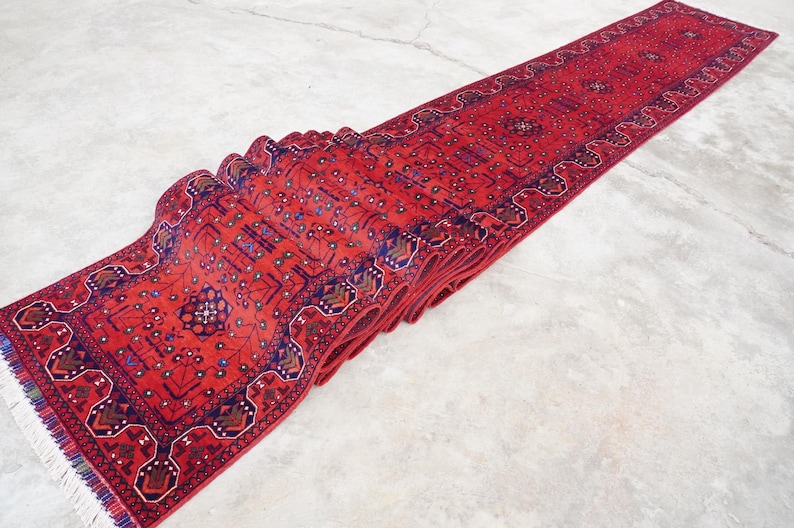 May include: A red runner rug with a traditional Persian design featuring intricate floral and geometric patterns in shades of blue, red, and white. The rug is folded in half and has a fringe on the ends.