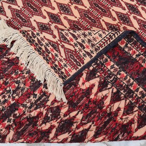 May include: Close-up of a rug with a geometric pattern in shades of red, black, and cream. The rug has a fringe border and is folded in half.