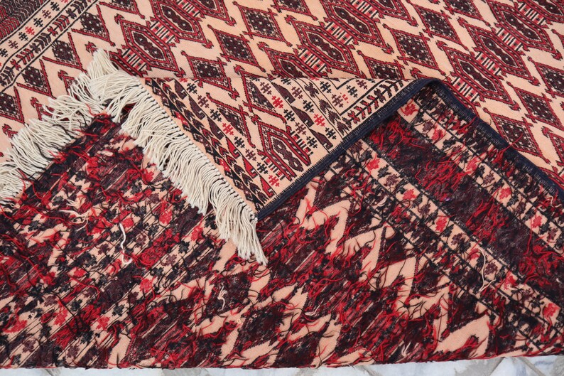 May include: Close-up of a rug with a geometric pattern in shades of red, black, and cream. The rug has a fringe border and is folded in half.
