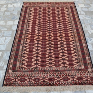 May include: A traditional rug with a red, black and white geometric pattern. The rug has a fringe border and is made of wool.