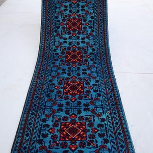 May include: A blue and red patterned runner rug with a geometric design. The rug has a fringe border.