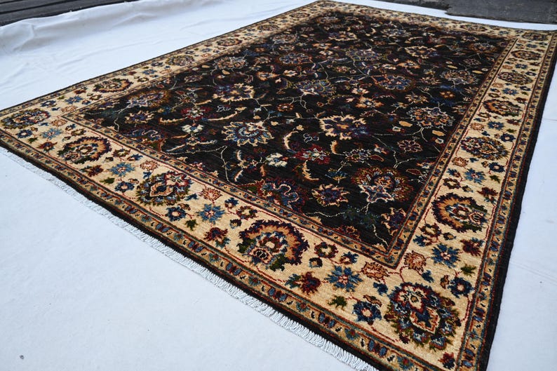 May include: A dark brown rug with a cream-coloured border. The rug has a floral pattern with intricate details. The rug is fringed on all sides.