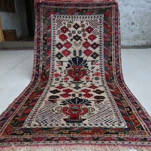 May include: A traditional Turkish rug with a cream background and intricate floral patterns in shades of red, blue, and green. The rug has a fringed edge and a central design featuring two stylized vases.