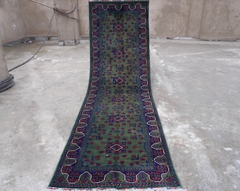 May include: A green, blue, and red runner rug with a traditional Persian design. The rug has a fringe border and is made of wool.