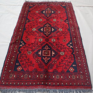 May include: A red rug with a blue and white geometric pattern. The rug has a fringe border.