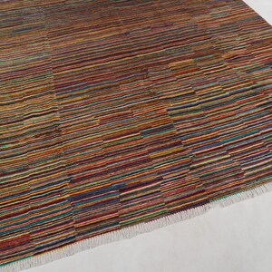 May include: A rectangular area rug featuring a dense pattern of thin, horizontal stripes in a vibrant palette of red, orange, yellow, blue, green, and purple. The rug has a textured surface and is finished with short, white fringe along the edges.