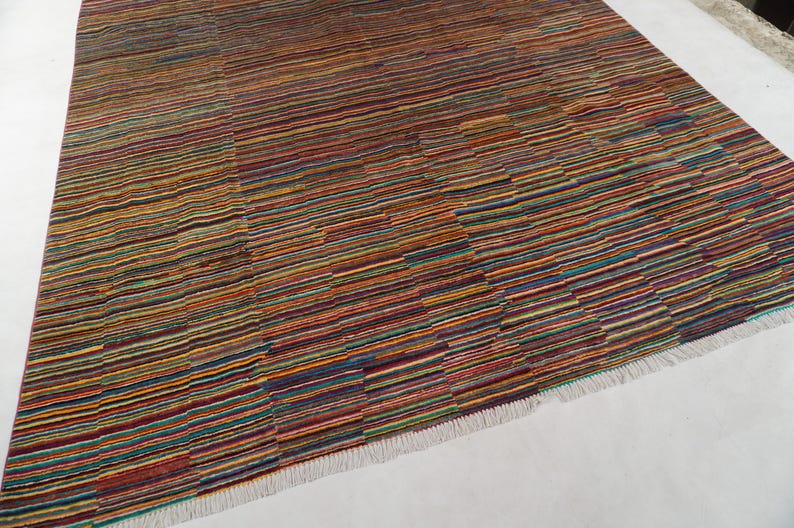 May include: A rectangular area rug featuring a dense pattern of thin, horizontal stripes in a vibrant palette of red, orange, yellow, blue, green, and purple. The rug has a textured surface and is finished with short, white fringe along the edges.