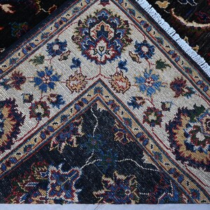 May include: Close-up of a rug with a white and black geometric pattern. The rug has a fringed border and features intricate floral designs in shades of blue, red, and gold.