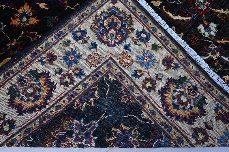 May include: Close-up of a rug with a white and black geometric pattern. The rug has a fringed border and features intricate floral designs in shades of blue, red, and gold.