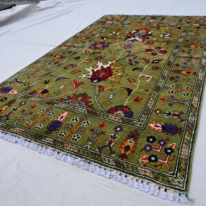 May include: A green rug with a floral pattern in shades of red, yellow, blue, and black. The rug has a fringe border.