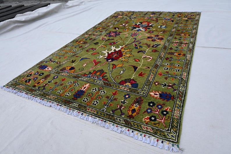 May include: A green rug with a floral pattern in shades of red, yellow, blue, and black. The rug has a fringe border.
