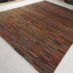 May include: A rectangular area rug featuring a dense pattern of thin, horizontal stripes in a multitude of colors including brown, orange, red, blue, green, and yellow. The rug has a flat-woven texture and short, light-colored fringe at the edges.