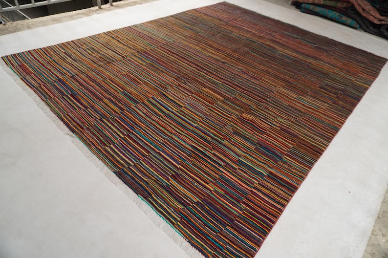 May include: A rectangular area rug featuring a dense pattern of thin, horizontal stripes in a multitude of colors including brown, orange, red, blue, green, and yellow. The rug has a flat-woven texture and short, light-colored fringe at the edges.
