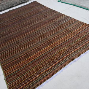 Pode incluir: Um tapete listrado com franjas brancas. O tapete &eacute; feito de uma variedade de cores, incluindo marrom, laranja, verde e azul.