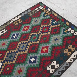 May include: A traditional Turkish rug with a geometric pattern in shades of red, green, blue, and brown. The rug has a fringe border.