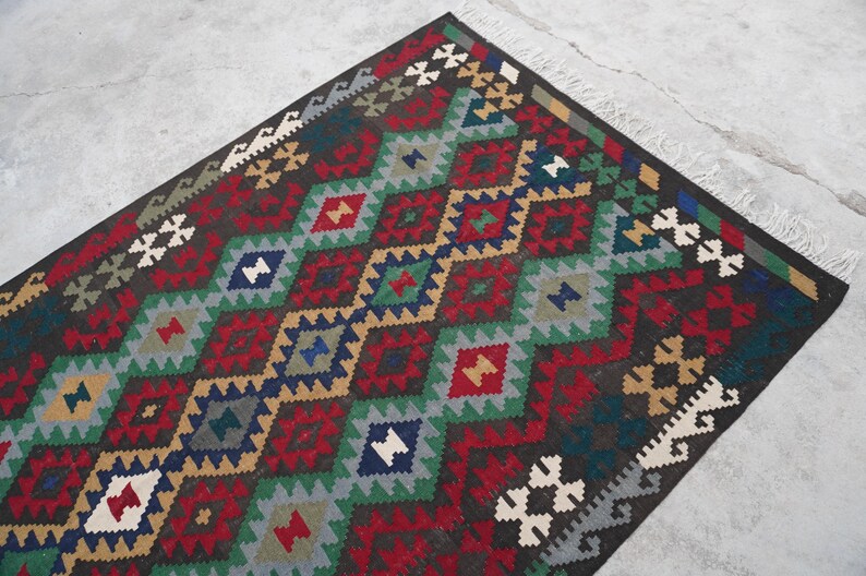 May include: A traditional Turkish rug with a geometric pattern in shades of red, green, blue, and brown. The rug has a fringe border.