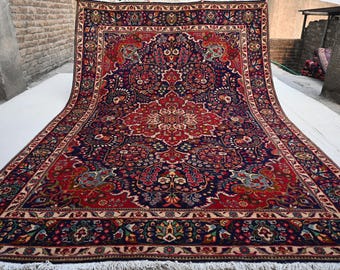 May include: A large, ornate Persian rug with a central medallion design. The rug features a rich color palette of deep red, navy blue, and cream, with intricate floral and geometric patterns. The rug has a fringed edge and is displayed outdoors.