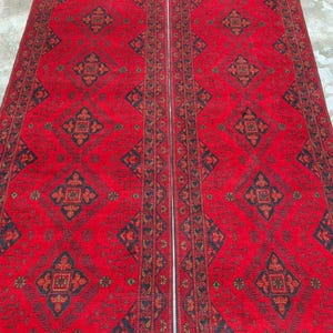 K&ouml;nnte beinhalten: Zwei passende rote Teppiche mit aufwendigen geometrischen Mustern in Schwarz und Braun. Die Teppiche weisen ein zentrales Rautenmuster und Bord&uuml;ren mit sich wiederholenden Motiven auf. Die Teppiche werden nebeneinander pr&auml;sentiert und zeigen ihr symmetrisches Design und ihre lebendige Farbe.