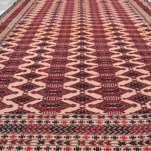 May include: A traditional rug with a geometric pattern in shades of red, black, and cream. The rug has a border with a repeating pattern of small triangles.