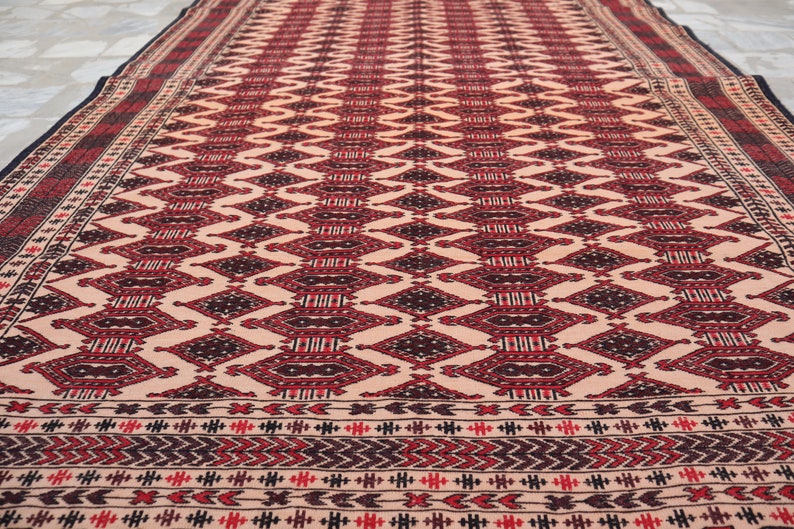 May include: A traditional rug with a geometric pattern in shades of red, black, and cream. The rug has a border with a repeating pattern of small triangles.