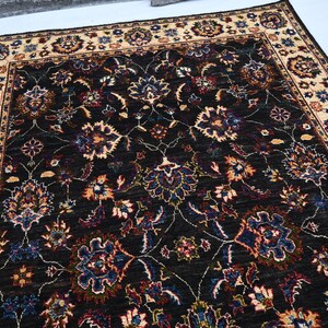 May include: A dark brown rug with a cream-coloured border. The rug features a floral pattern with intricate details in shades of blue, red, and cream.