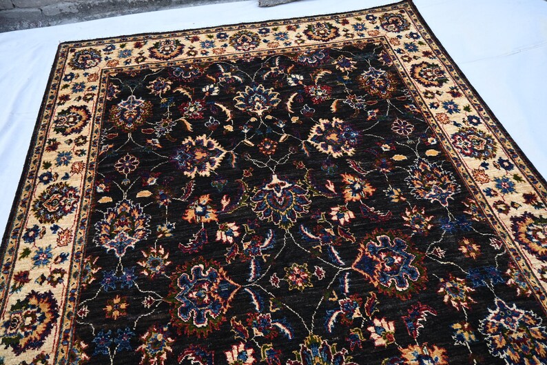 May include: A dark brown rug with a cream-coloured border. The rug features a floral pattern with intricate details in shades of blue, red, and cream.