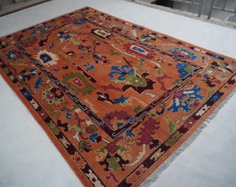 May include: An orange rectangular rug with a detailed floral pattern in shades of blue, green, red, and white. The rug has a dark border and fringe along the edges. The rug is likely made of wool or a similar material.
