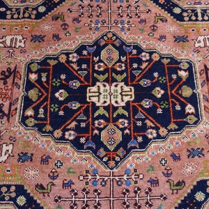 May include: An intricately patterned rug with a central navy blue medallion featuring floral and geometric designs. The rug has a dusty rose field with a navy blue border and accents of green, orange, and white. The rug's design is symmetrical and detailed.