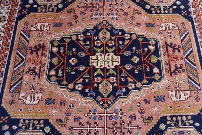 May include: An intricately patterned rug with a central navy blue medallion featuring floral and geometric designs. The rug has a dusty rose field with a navy blue border and accents of green, orange, and white. The rug's design is symmetrical and detailed.
