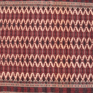 May include: A traditional rug with a cream background and a repeating geometric pattern in shades of red, black, and white. The rug has a border with a smaller geometric pattern.