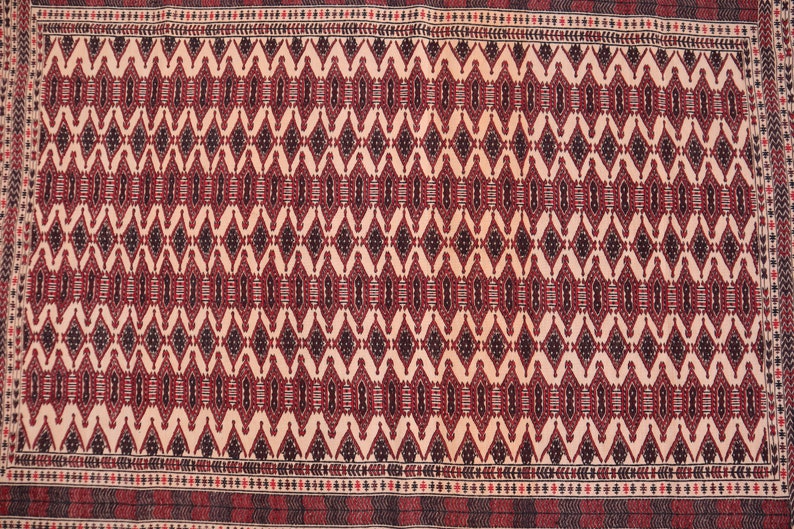 May include: A traditional rug with a cream background and a repeating geometric pattern in shades of red, black, and white. The rug has a border with a smaller geometric pattern.