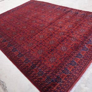 May include: A red rug with a blue and red patterned border. The rug has a traditional design with intricate details.