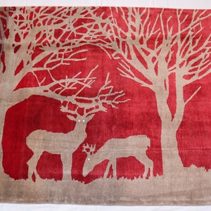 May include: A rectangular red rug with a beige tree and deer design. The rug features a detailed illustration of trees and two deer. The edges are finished with a fringe.