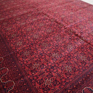 May include: A red rug with a geometric pattern in shades of blue and gold. The rug has a border with a repeating design.