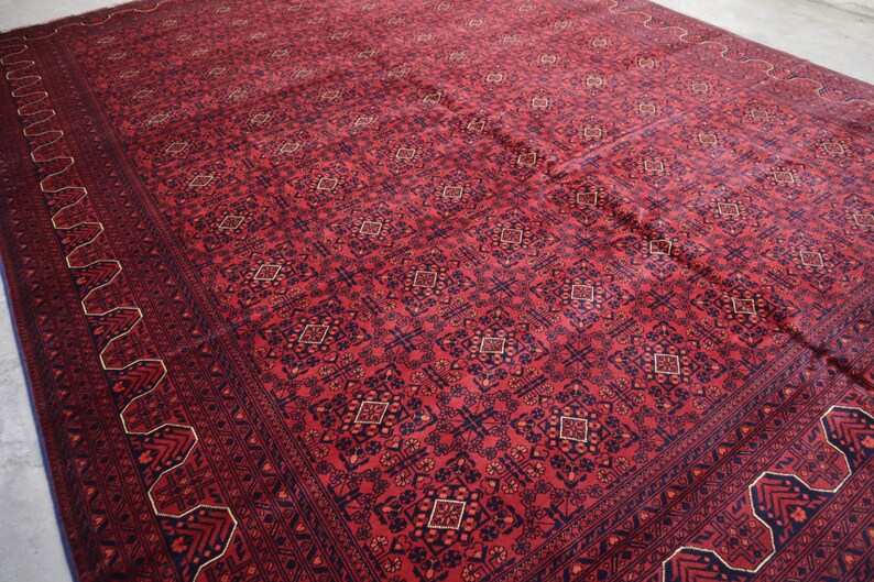 May include: A red rug with a geometric pattern in shades of blue and gold. The rug has a border with a repeating design.
