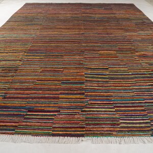 May include: A rectangular area rug featuring a dense, multi-colored horizontal striped pattern. The design consists of thin, varied bands in shades of red, orange, yellow, blue, green, and purple, finished with a white fringe along the bottom edge.