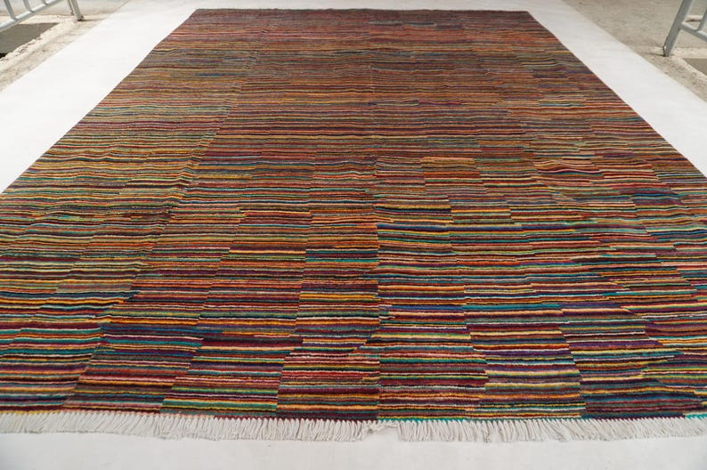 May include: A rectangular area rug featuring a dense, multi-colored horizontal striped pattern. The design consists of thin, varied bands in shades of red, orange, yellow, blue, green, and purple, finished with a white fringe along the bottom edge.