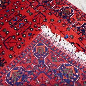 May include: A red rug with a geometric pattern in blue, green, and white. The rug has a fringe border.