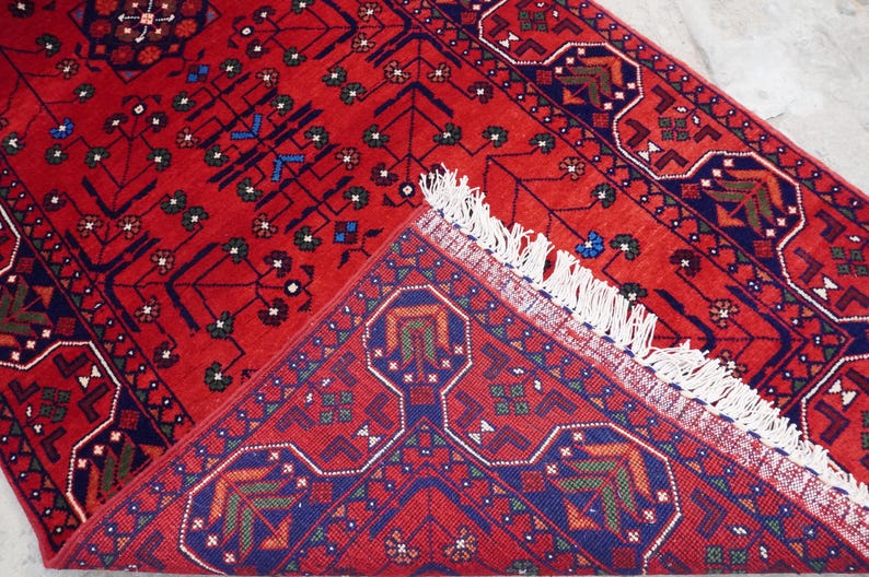 May include: A red rug with a geometric pattern in blue, green, and white. The rug has a fringe border.