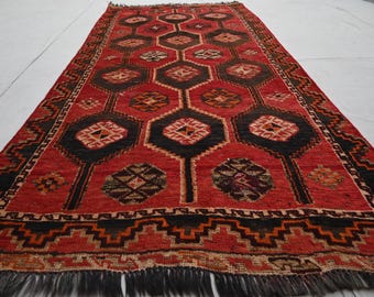 May include: A red and black patterned rug with a geometric design. The rug has a fringe border and is made of wool.