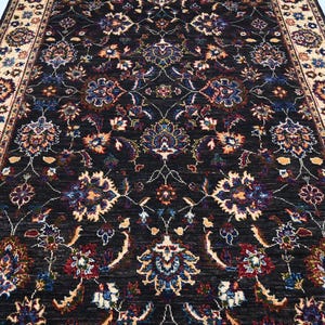 May include: A black rug with a floral pattern in shades of cream, red, blue, and green. The rug has a border with a cream background and a floral pattern in shades of red, blue, and green.