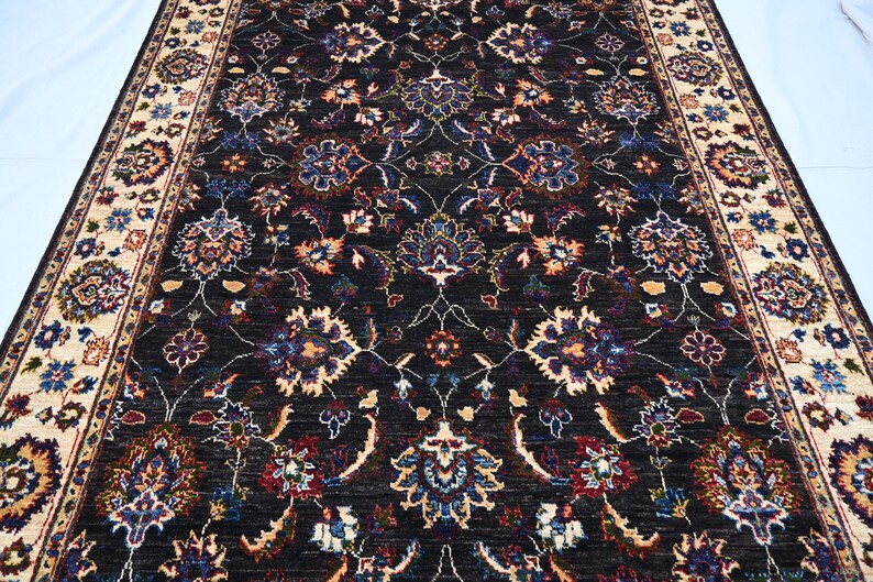 May include: A black rug with a floral pattern in shades of cream, red, blue, and green. The rug has a border with a cream background and a floral pattern in shades of red, blue, and green.