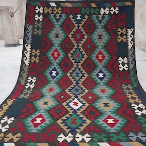 May include: A traditional hand-woven rug with a geometric pattern in shades of red, green, blue, and white on a dark brown background.