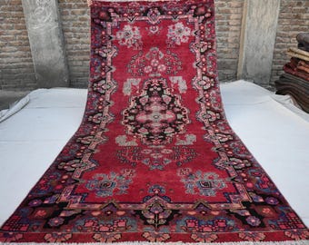 May include: A vintage red rug with a floral pattern and intricate border. The rug has a faded look and is made of wool.