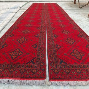 K&ouml;nnte beinhalten: Zwei lange, rechteckige rote Teppiche mit komplizierten geometrischen Mustern in Schwarz und Orange. Die Teppiche haben an den kurzen Enden einen Fransen. Die Teppiche liegen nebeneinander und scheinen handgefertigt zu sein.
