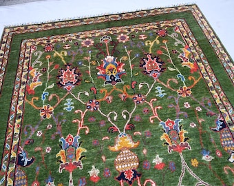 May include: A green rug with a floral pattern in shades of red, blue, yellow, and white. The rug has a border with a geometric pattern.