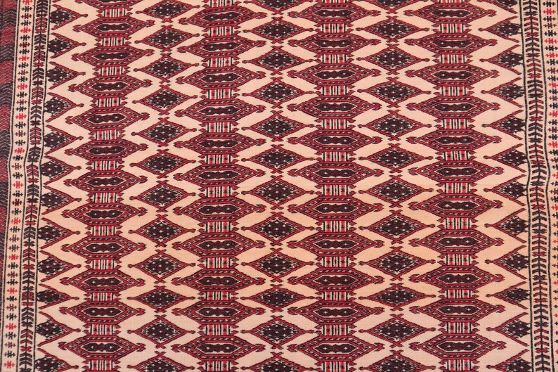 May include: A beige rug with a repeating geometric pattern in shades of red and black. The pattern features diamond shapes with intricate details.