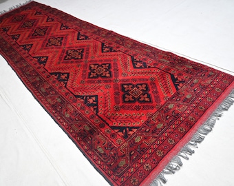 Puede incluir: Una alfombra de pasillo roja y negra con un patrón geométrico. La alfombra tiene flecos en ambos extremos.